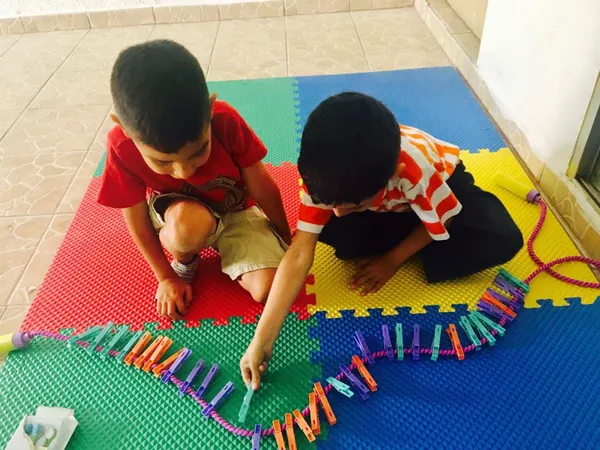 Dos niños colocando pinzas de colores en una cuerda